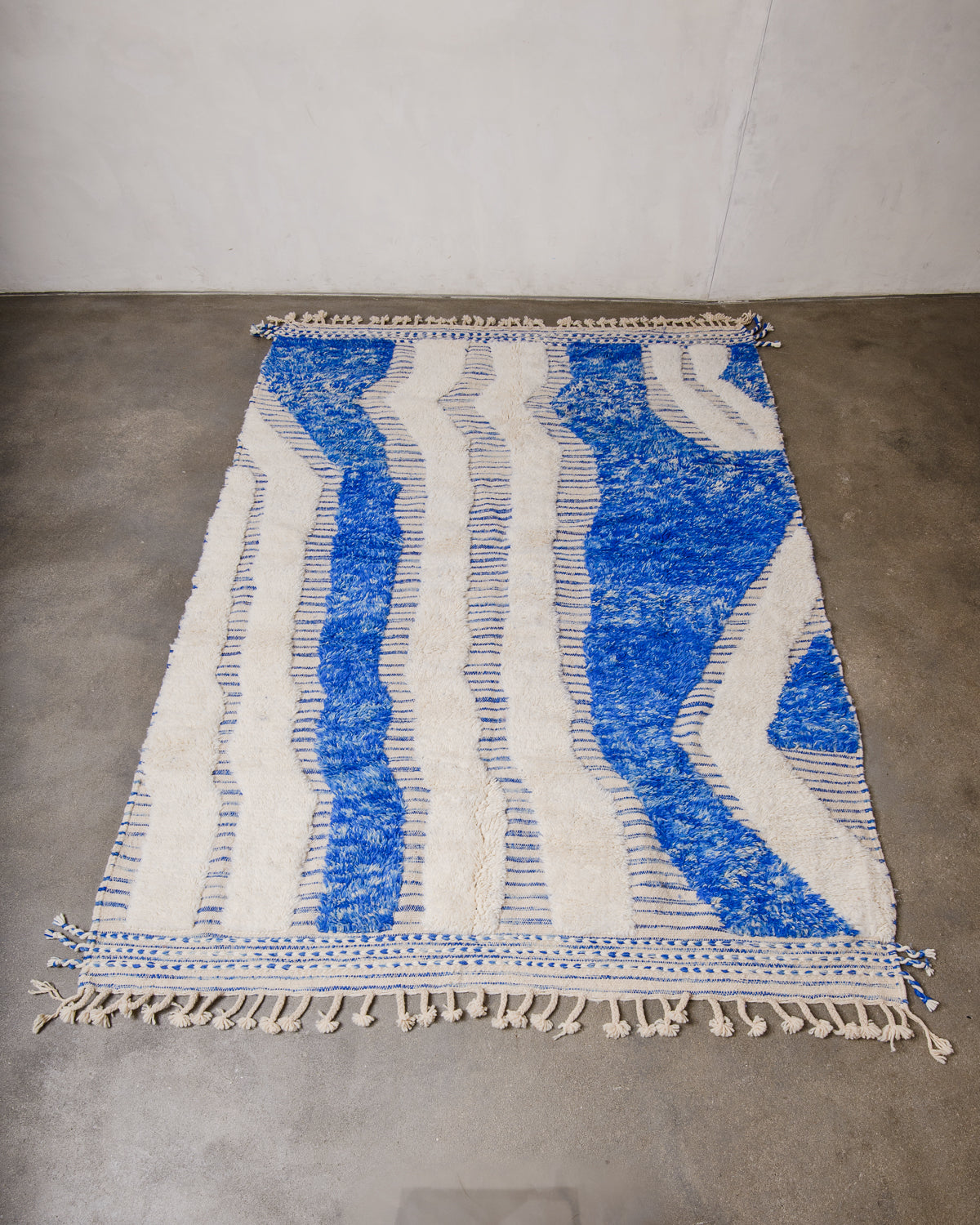 Cream and blue wool rug with a design made of a mix of high pile and flat woven areas laying flat on concrete floor.