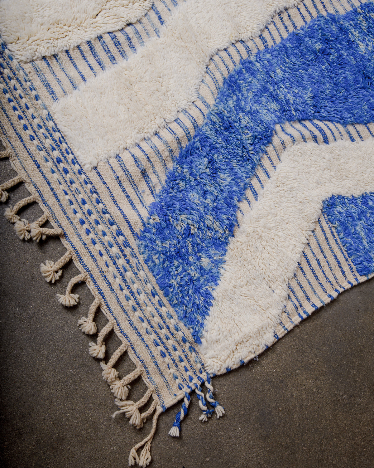 Corner of wool rug with tightly woven end and natural wool tassels. 