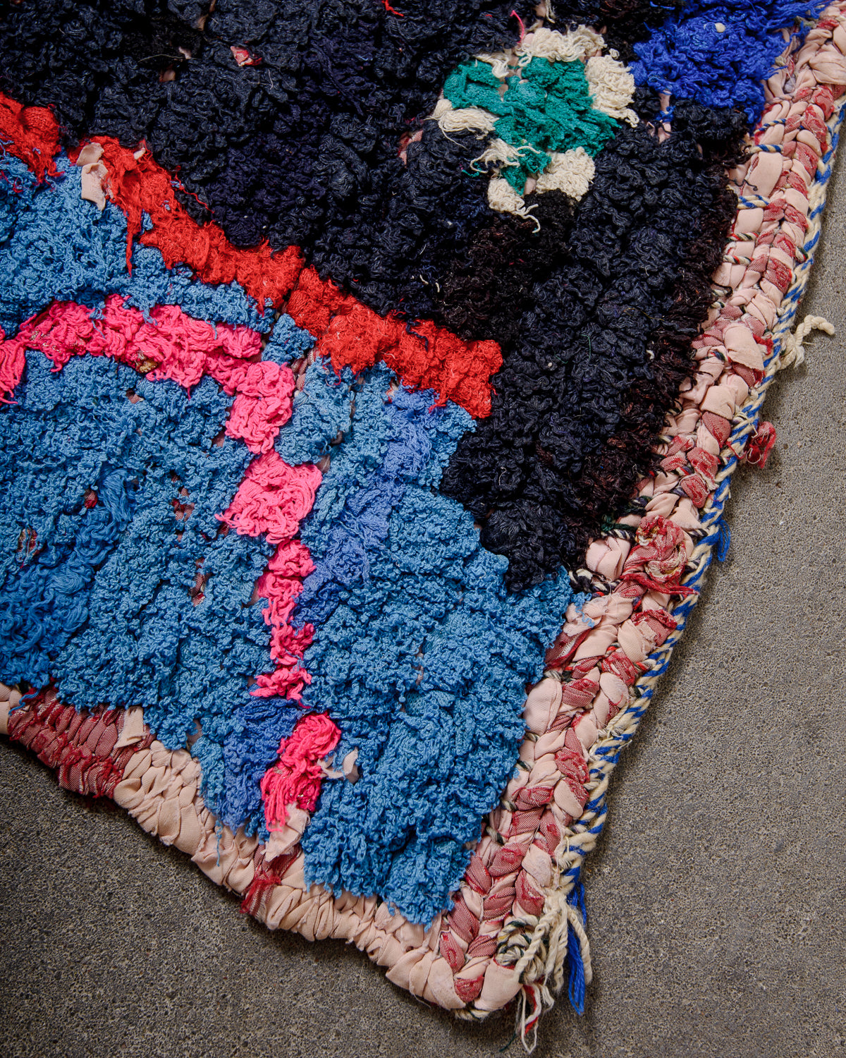 Corner of vintage boucherouite rug featuring edges made of woven cloth remnants. 