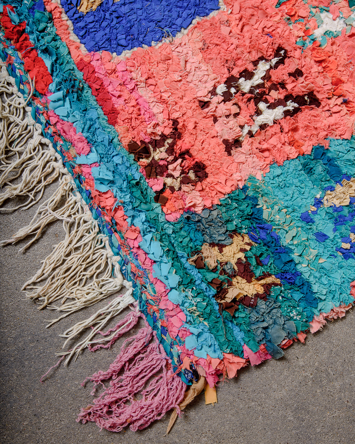 Corner of Berberlin vintage Boucherouite runner displaying cotton tassels in pink and white.