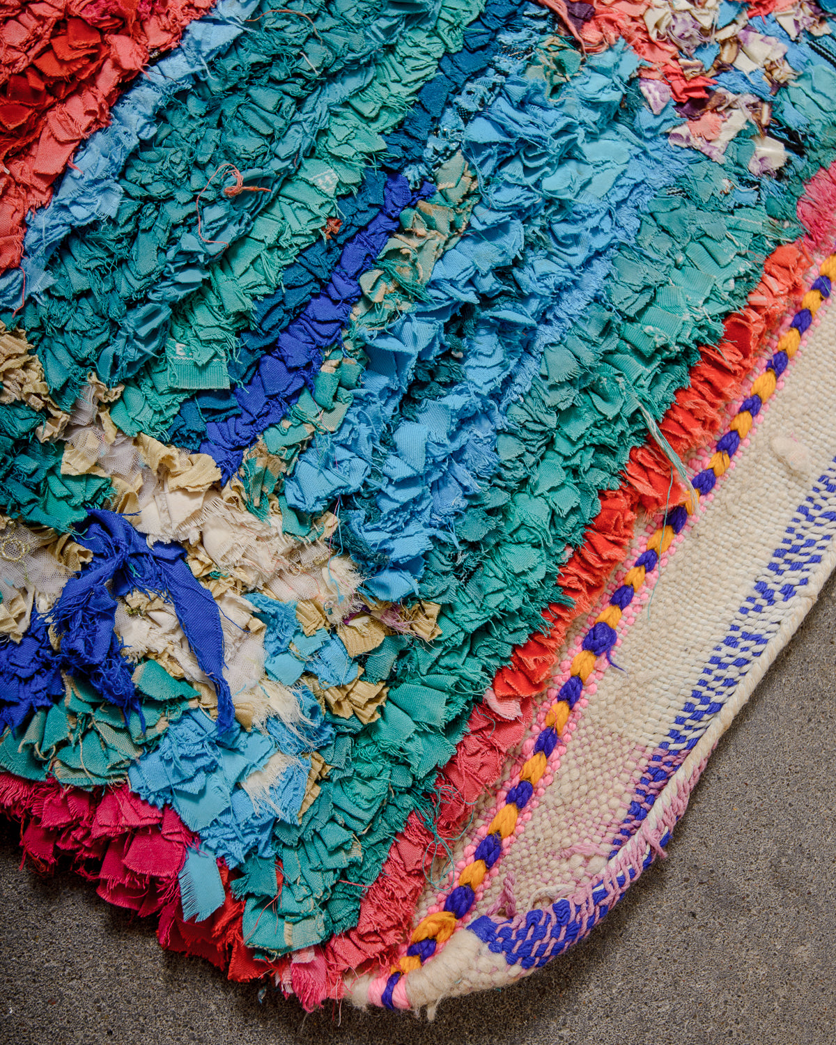 Corner of Boucherouite rug with woven end made up of blue fabric remnants and cream wool.