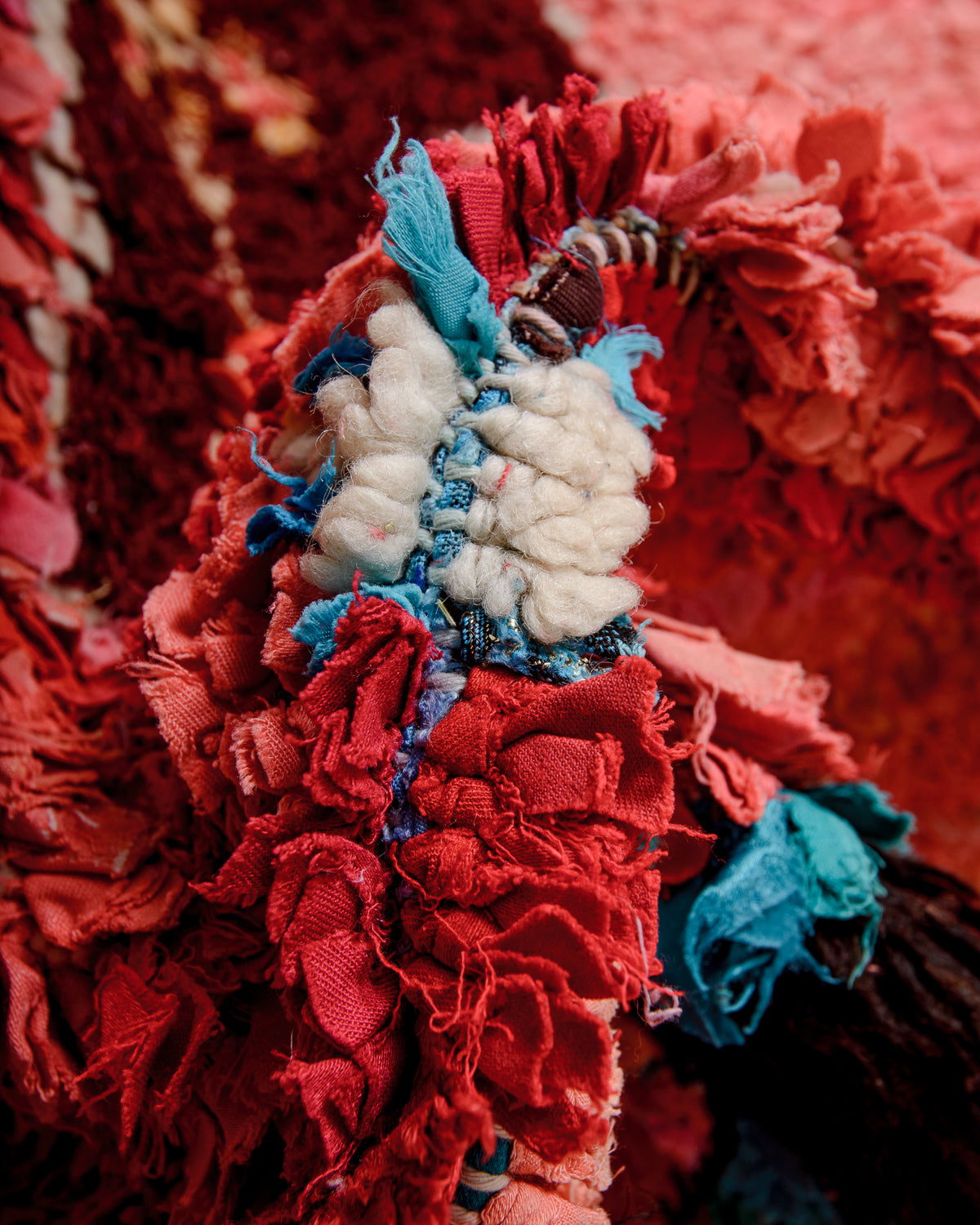 Close up showing wool, cotton and fabric remnants, in shades of red and white, used to make up this Boucherouite "rag rug".