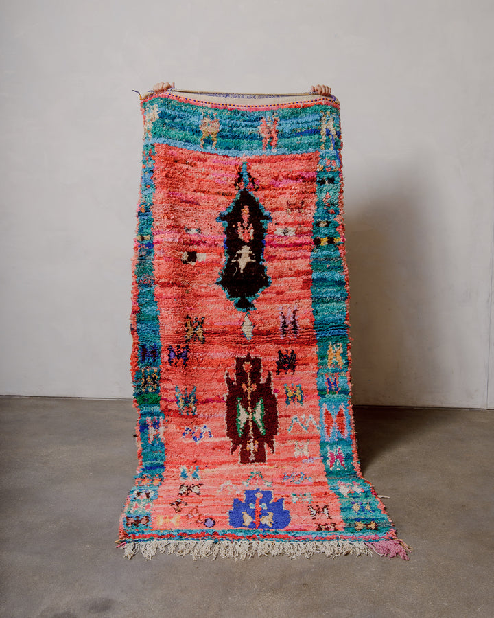 Berberlin vintage Boucherouite runner rug being held up against a white wall. 