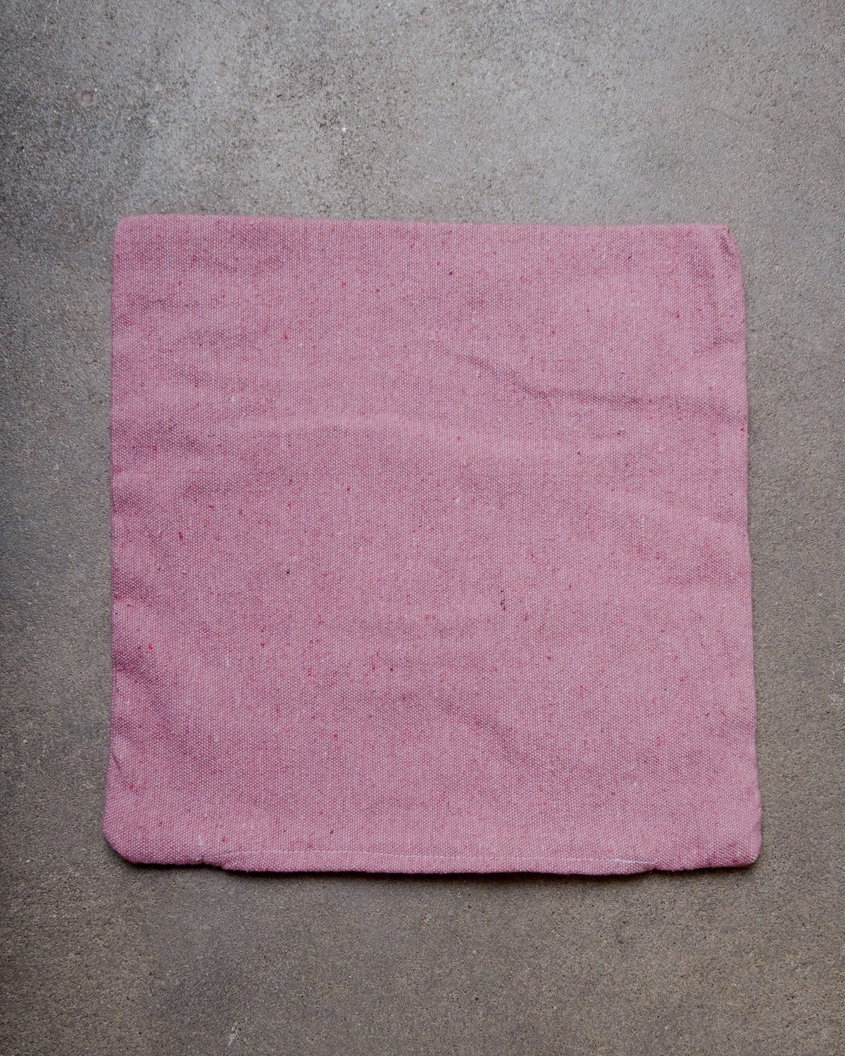 Back of pink wool cushion cover laying on concrete floor.