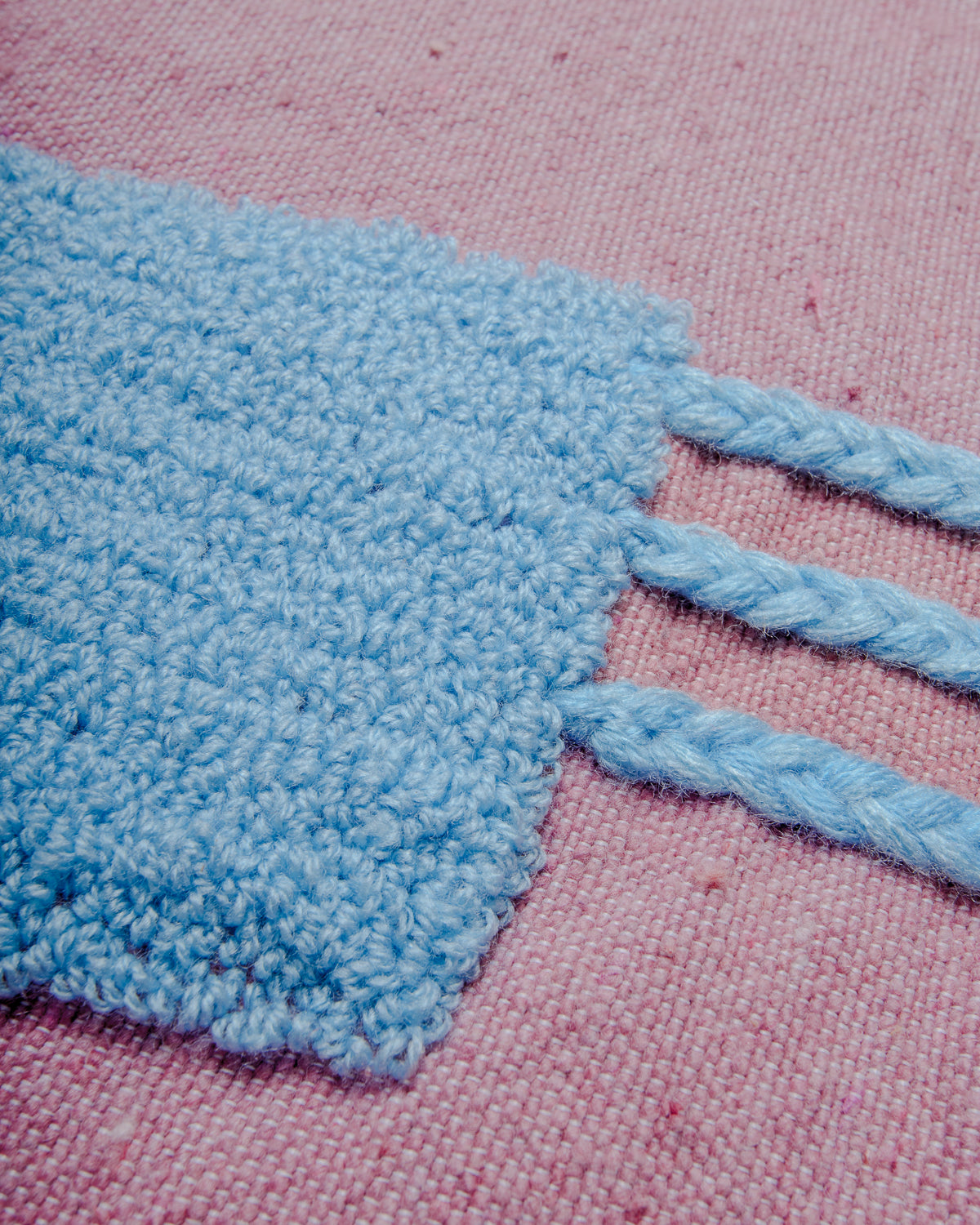 Detail of blue embroidered design on pink wool cushion cover.