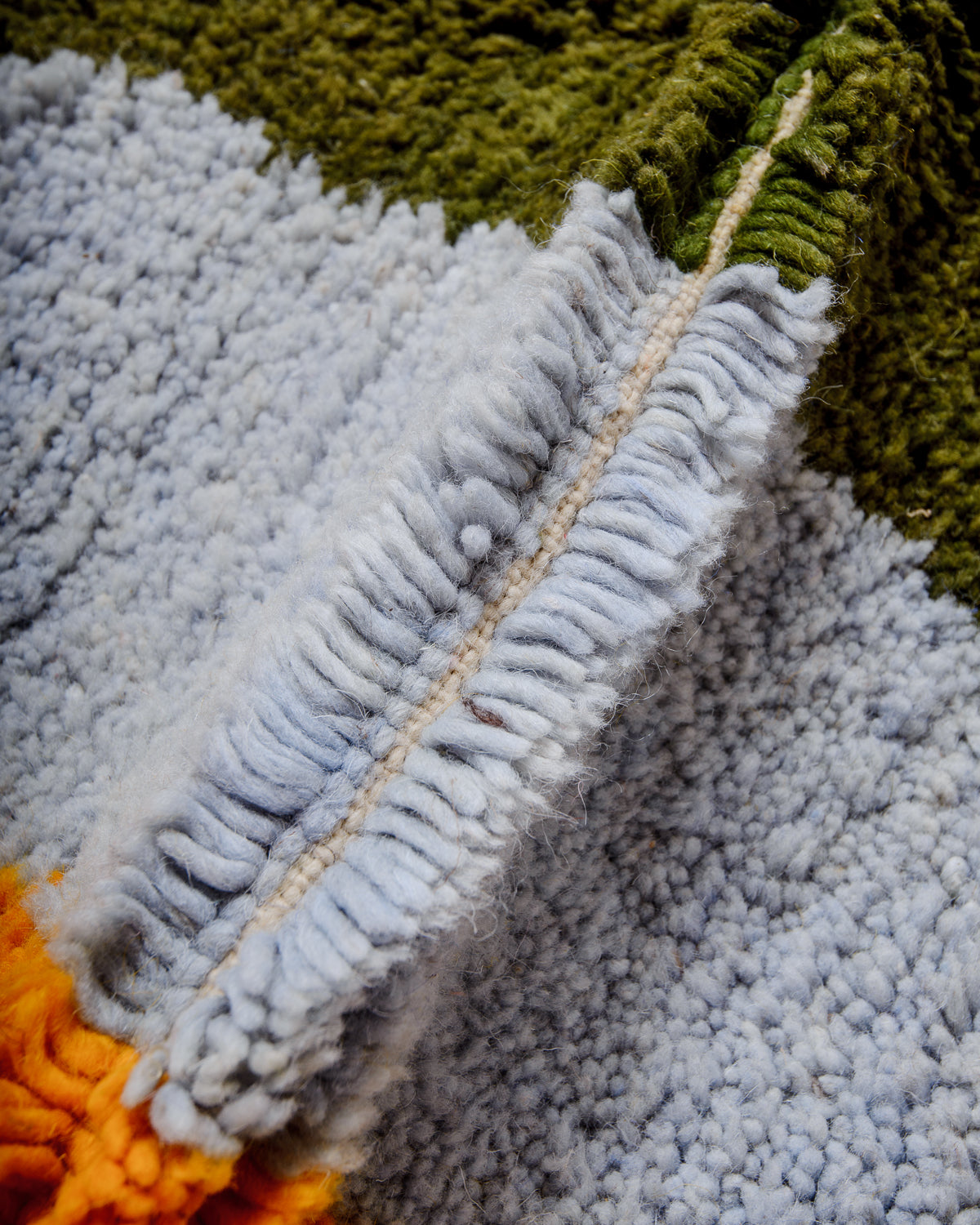 Detail of blue, olive and orange coloured wool of Berberlin finest Beniourain rug showing thick wool pile and dense knots.