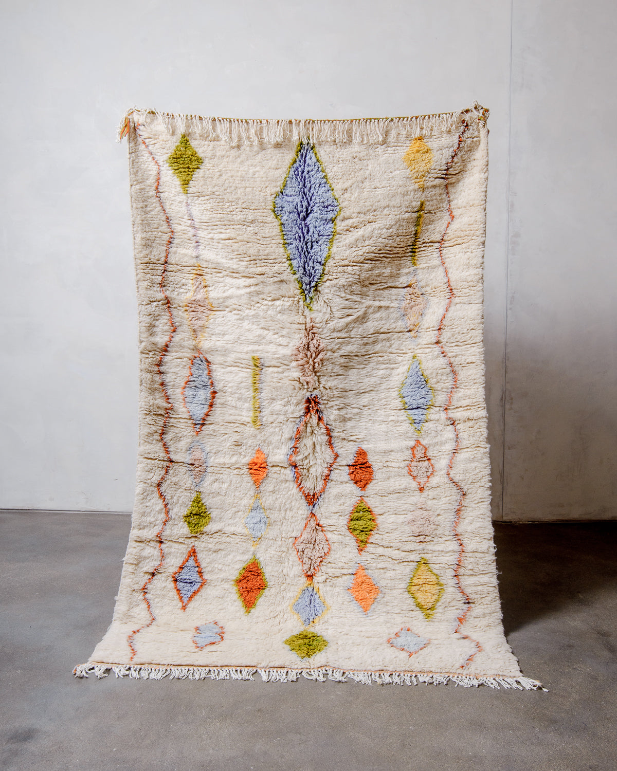 Berberlin Finest Rug made of plush cream wool with a charming design being held up in front of a white wall. 