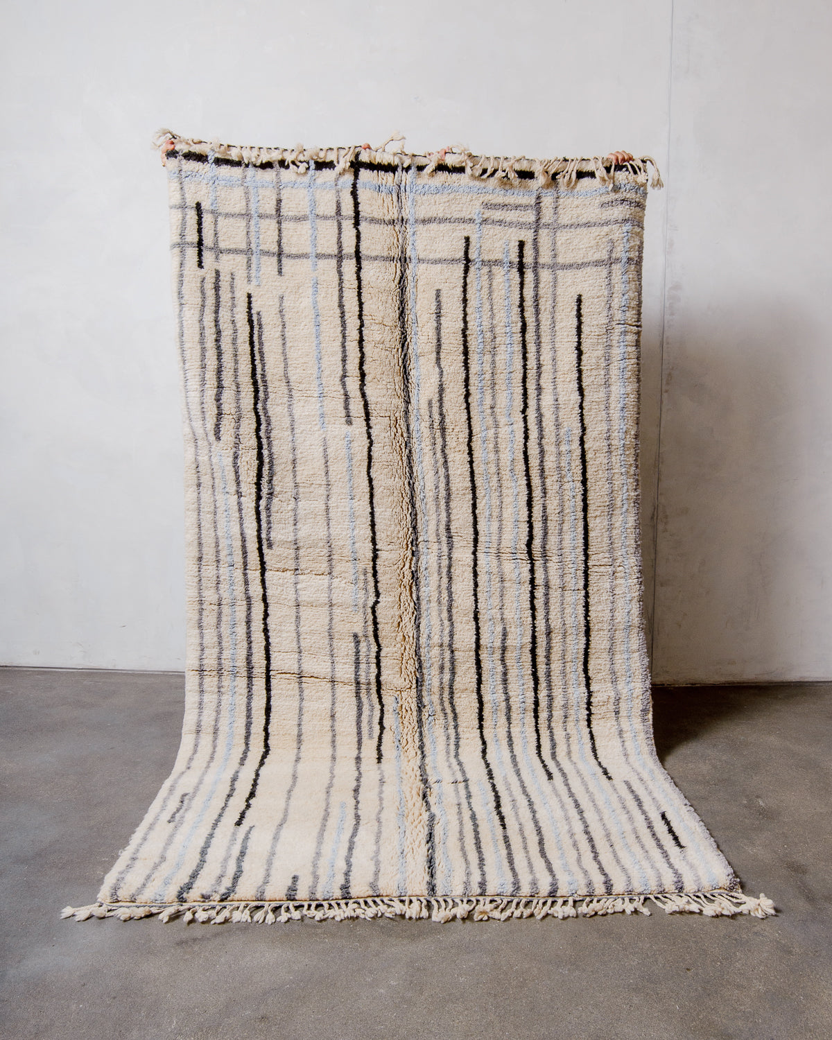 Berberlin Finest Rug made of heavy wool pile being held up in front of a white wall and concrete floor. 