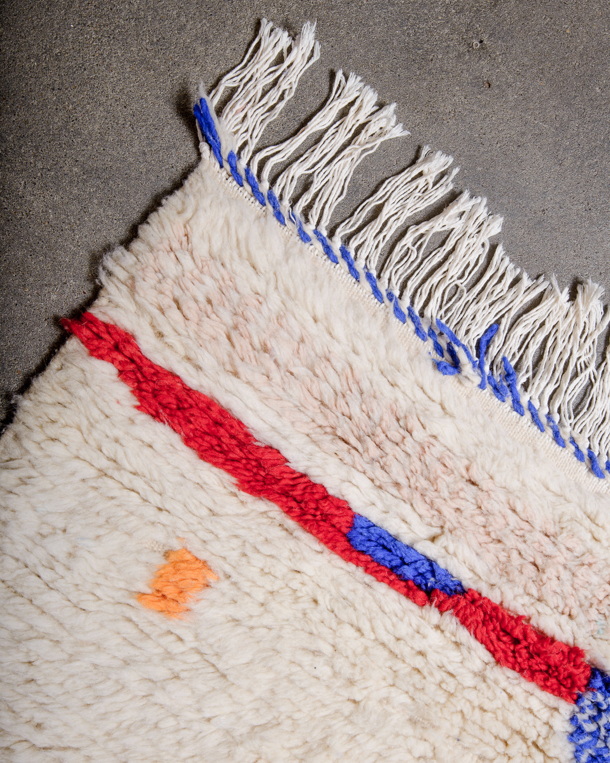 Corner of rug made of thick, fluffy wool pile with white cotton tassels. 