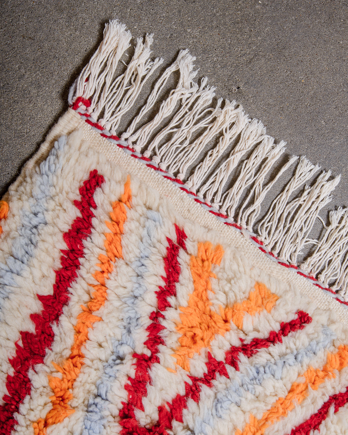 Corner of rug made of thick, fluffy wool pile with white cotton tassels. 
