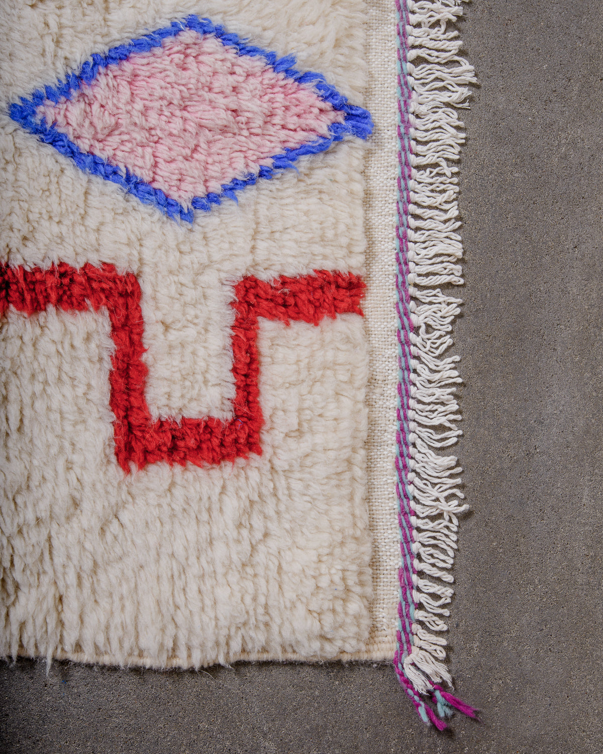 Corner of rug made of thick, fluffy wool pile with white cotton tassels. 