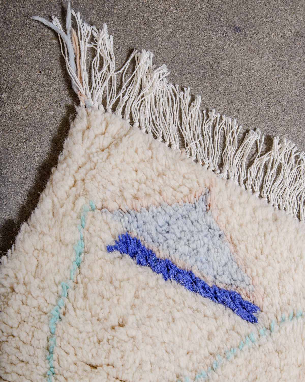 Corner of rug made of thick, fluffy wool pile with white cotton tassels. 