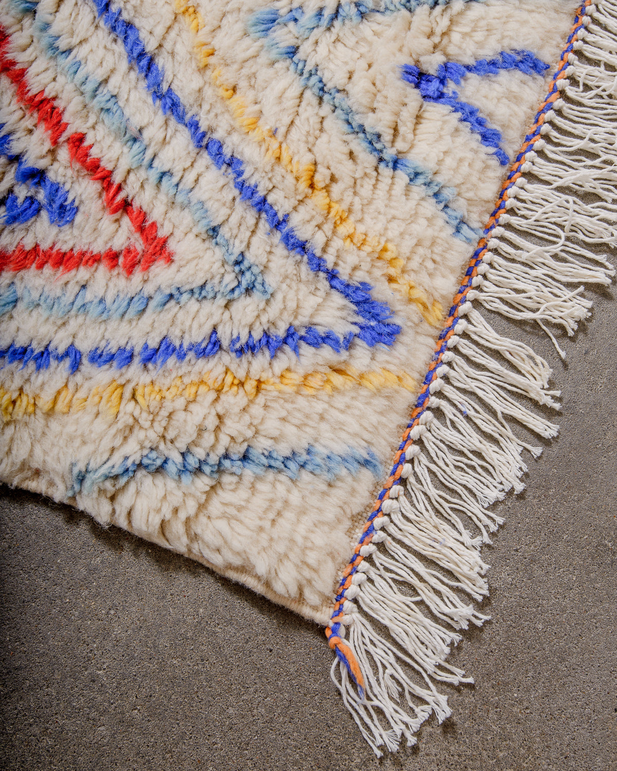 Corner of rug made of thick, fluffy wool pile with white cotton tassels. 