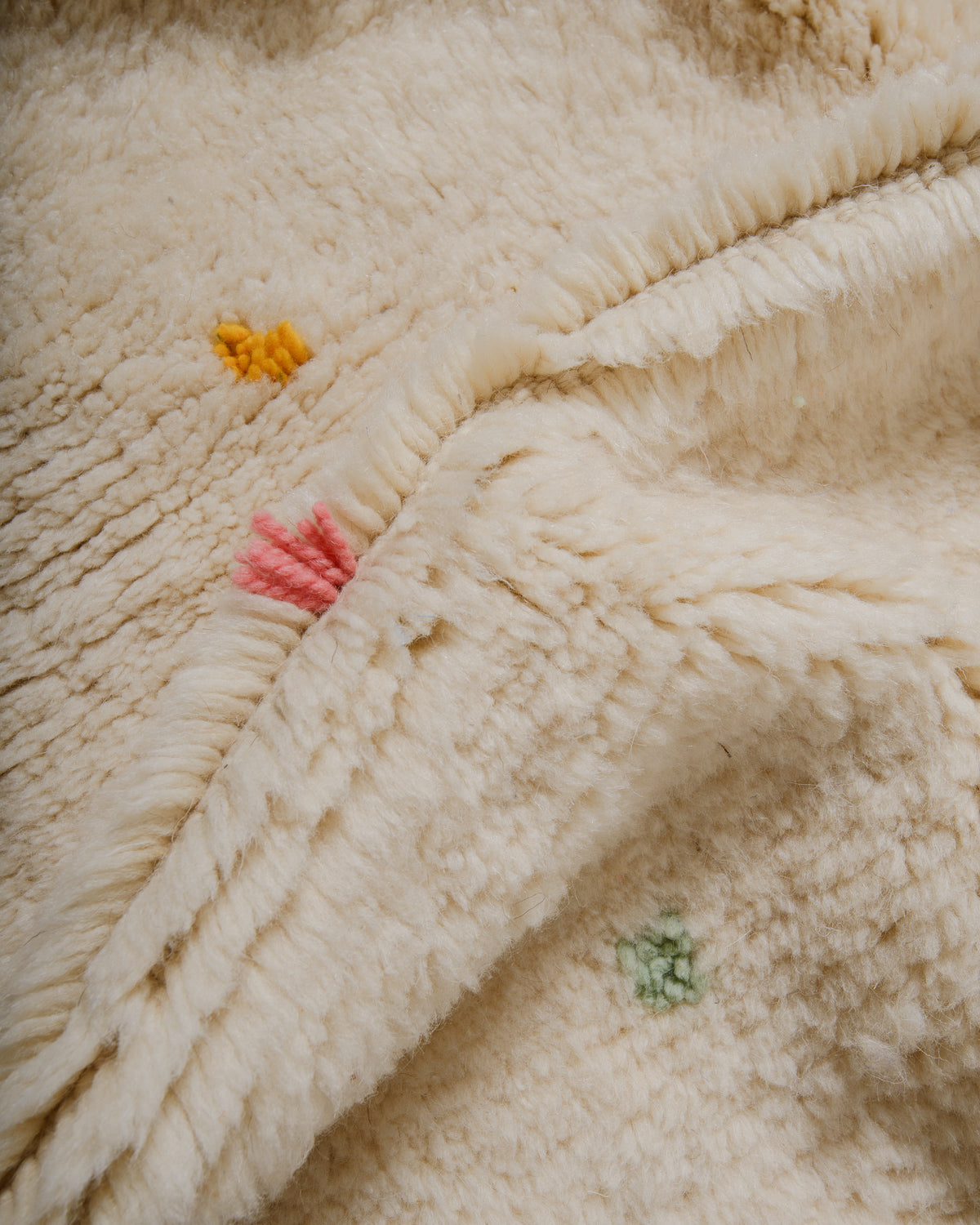 Close-up of textured cream rug with dense pile and colourful dots. 