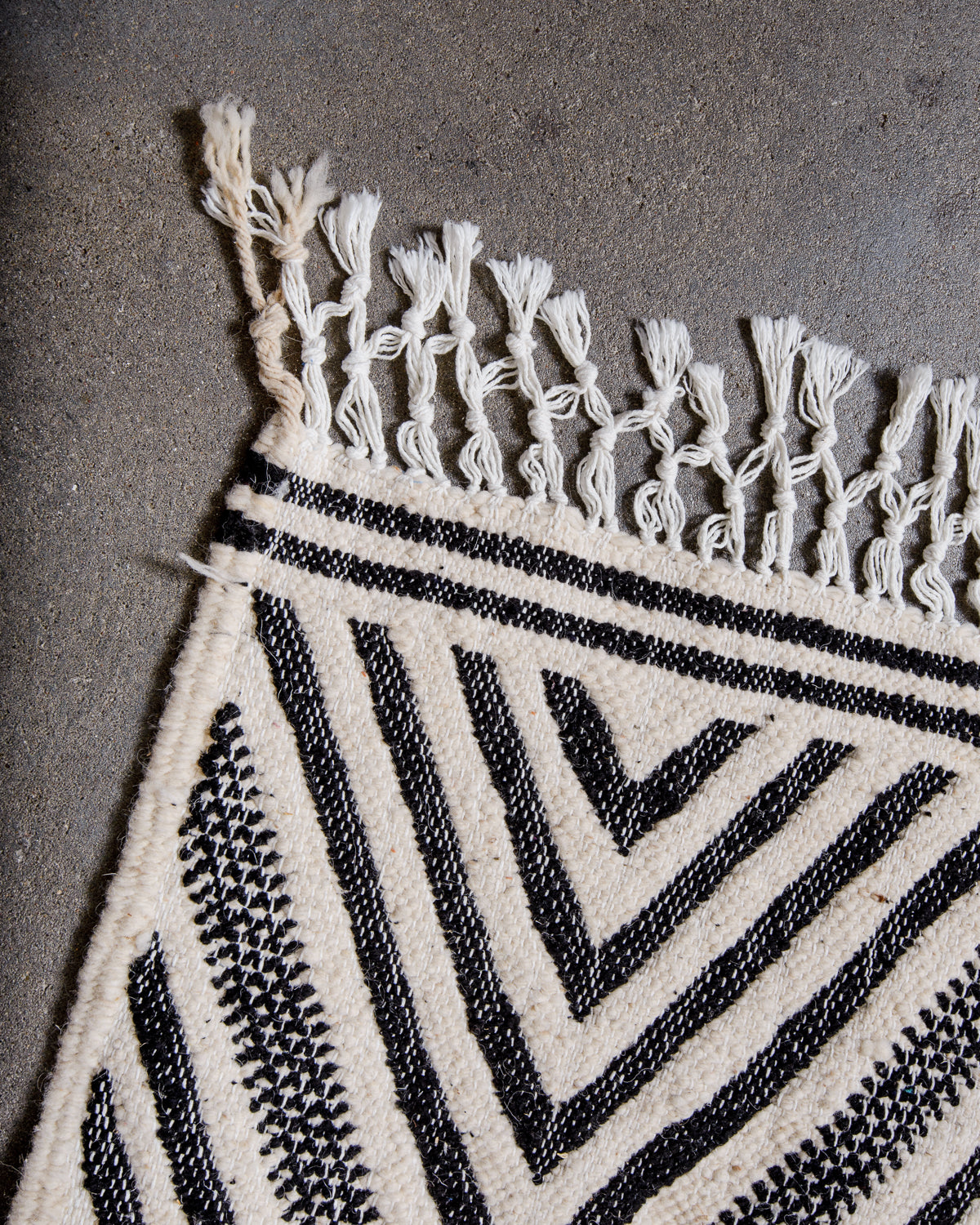 Corner of Kelim rug with white cotton tassels.