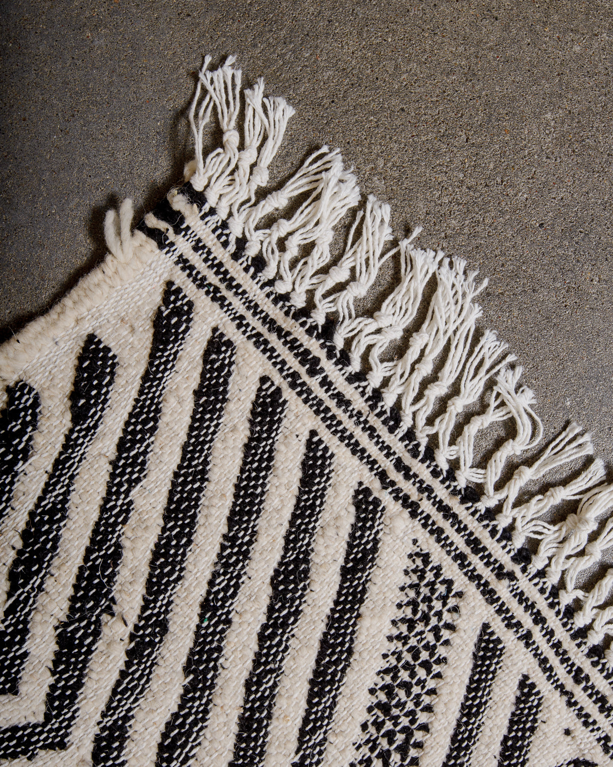 Corner of Kelim rug made of black and white wool with white cotton tassels. 