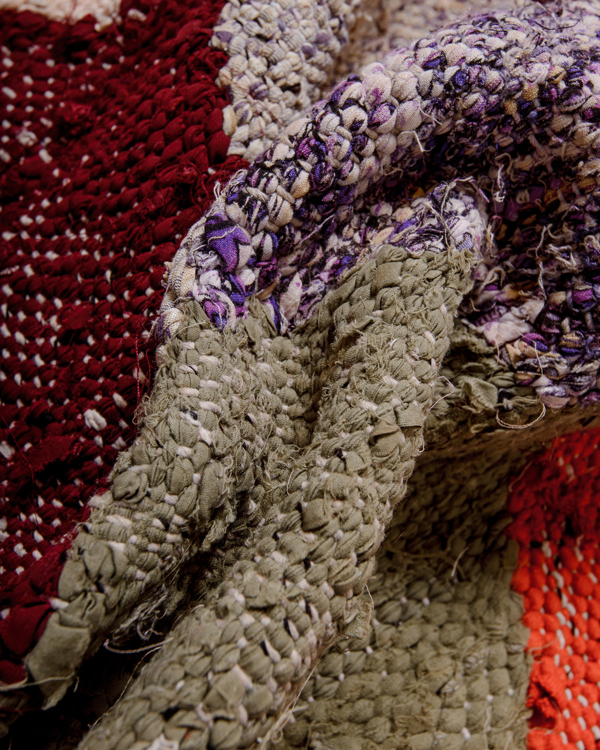 Texture of vintage Kelim rug made of recycled cotton and fabric remnants, in shades of red, burgundy, purple and khaki.