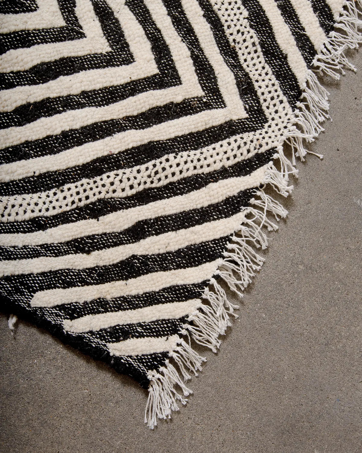Corner of black and white Kelim rug finished with short white cotton tassels.
