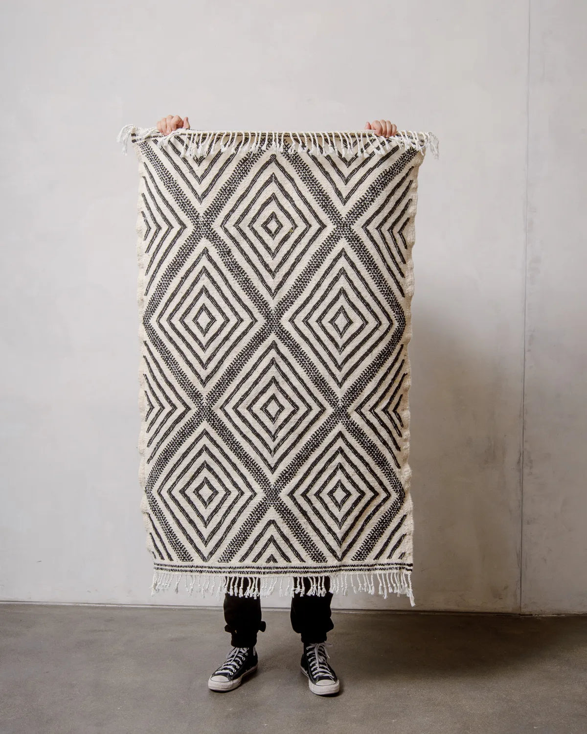 Small Berberlin Kelim Rug in black and white being held up in front of a white wall.