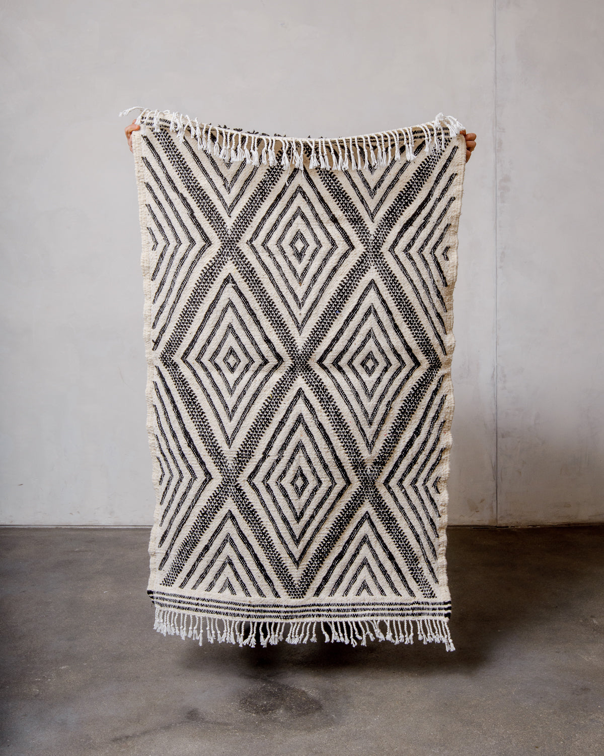 Small Berberlin Kelim Rug in black and white being held up in front of a white wall.