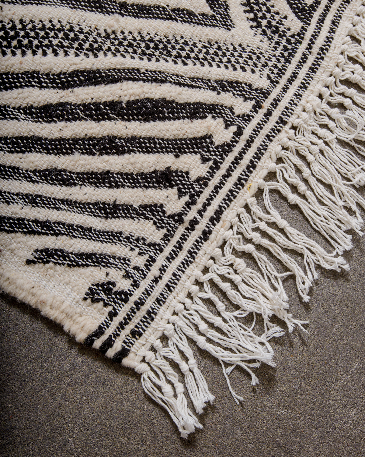 Corner of Kelim rug made of black and white wool with white cotton tassels. 