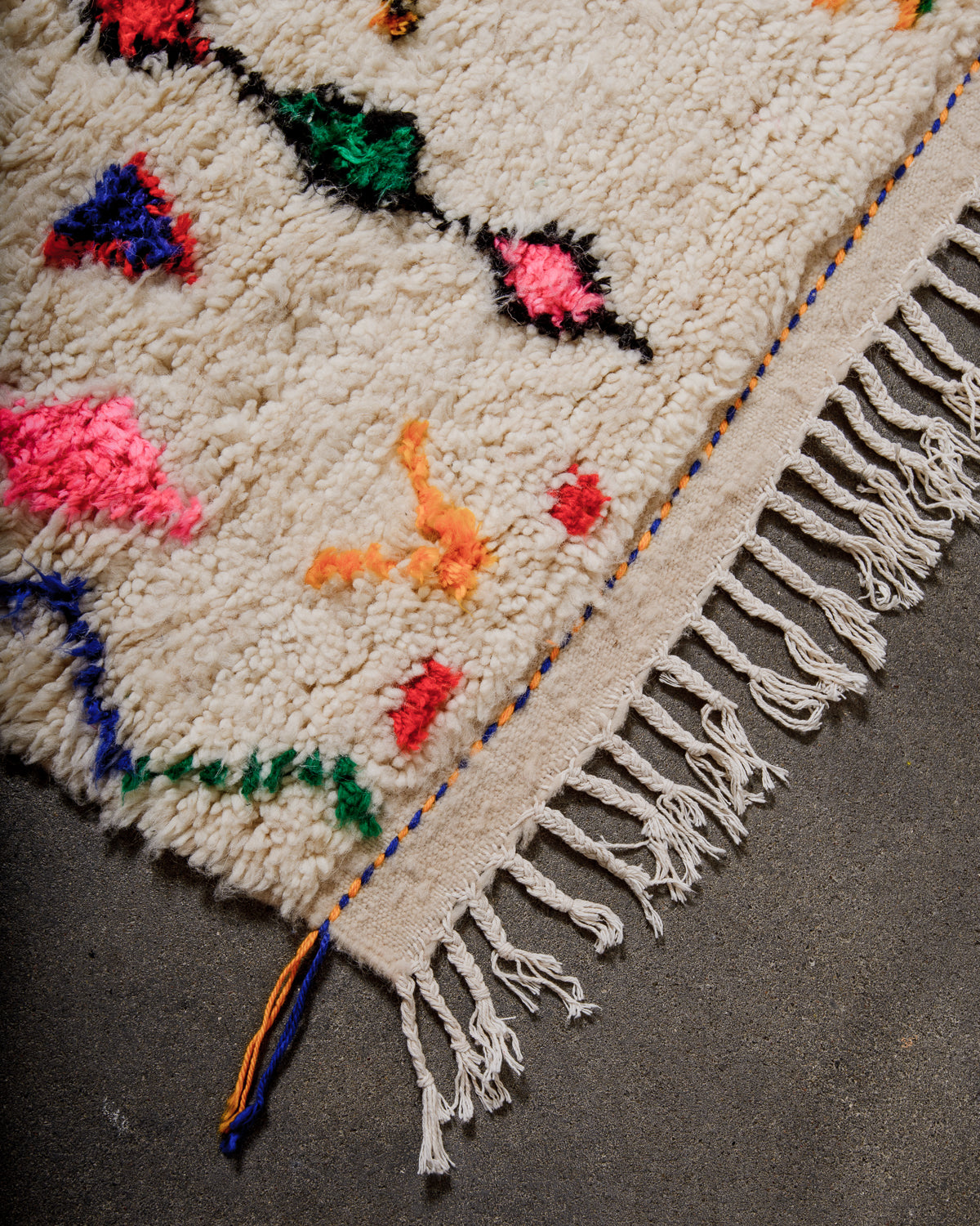 Corner of Azilal rug with a tightly woven edge and white cotton tassels along the end.