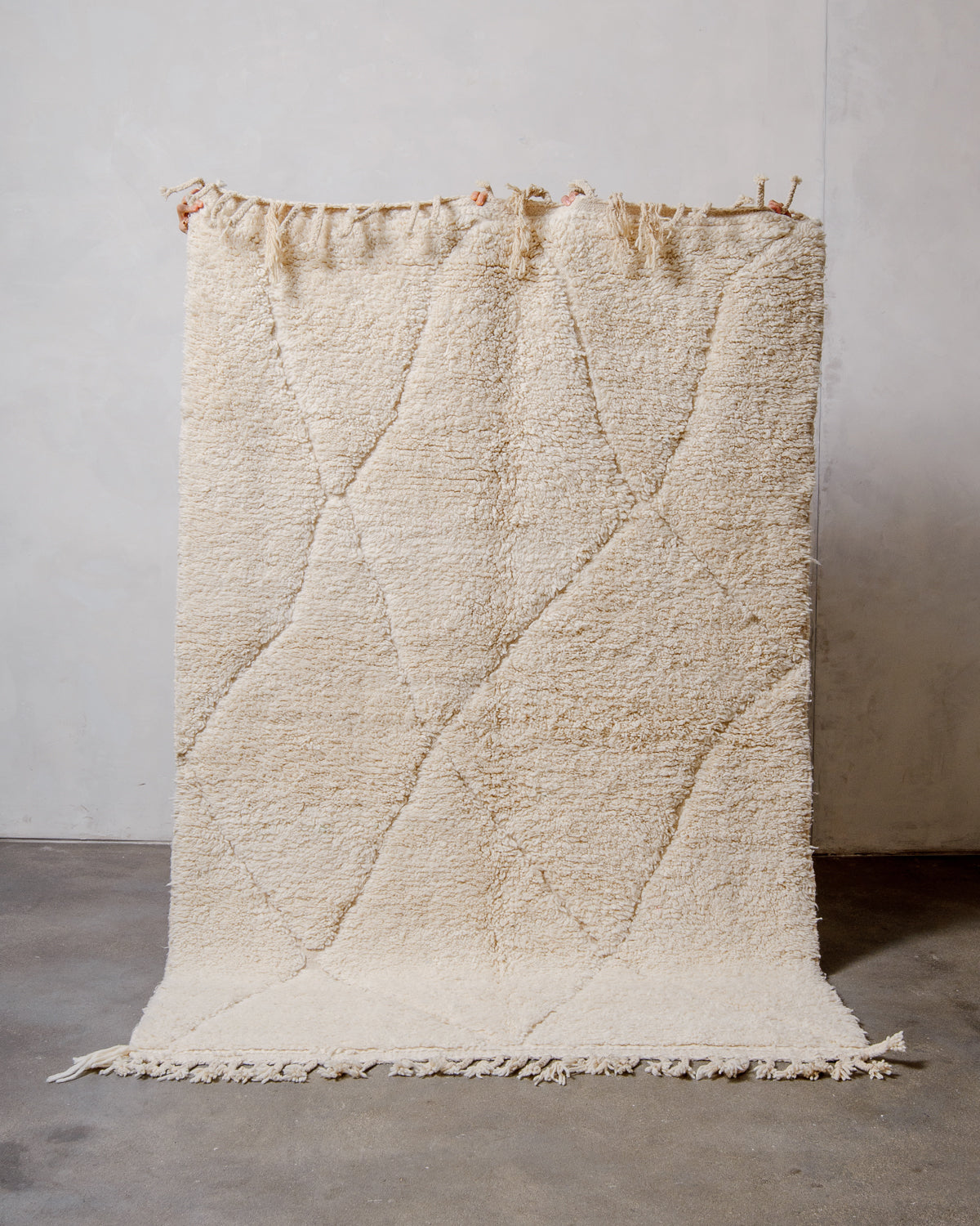 Berberlin Beniourain Rug made of cream wool being held up in front of a white wall. 