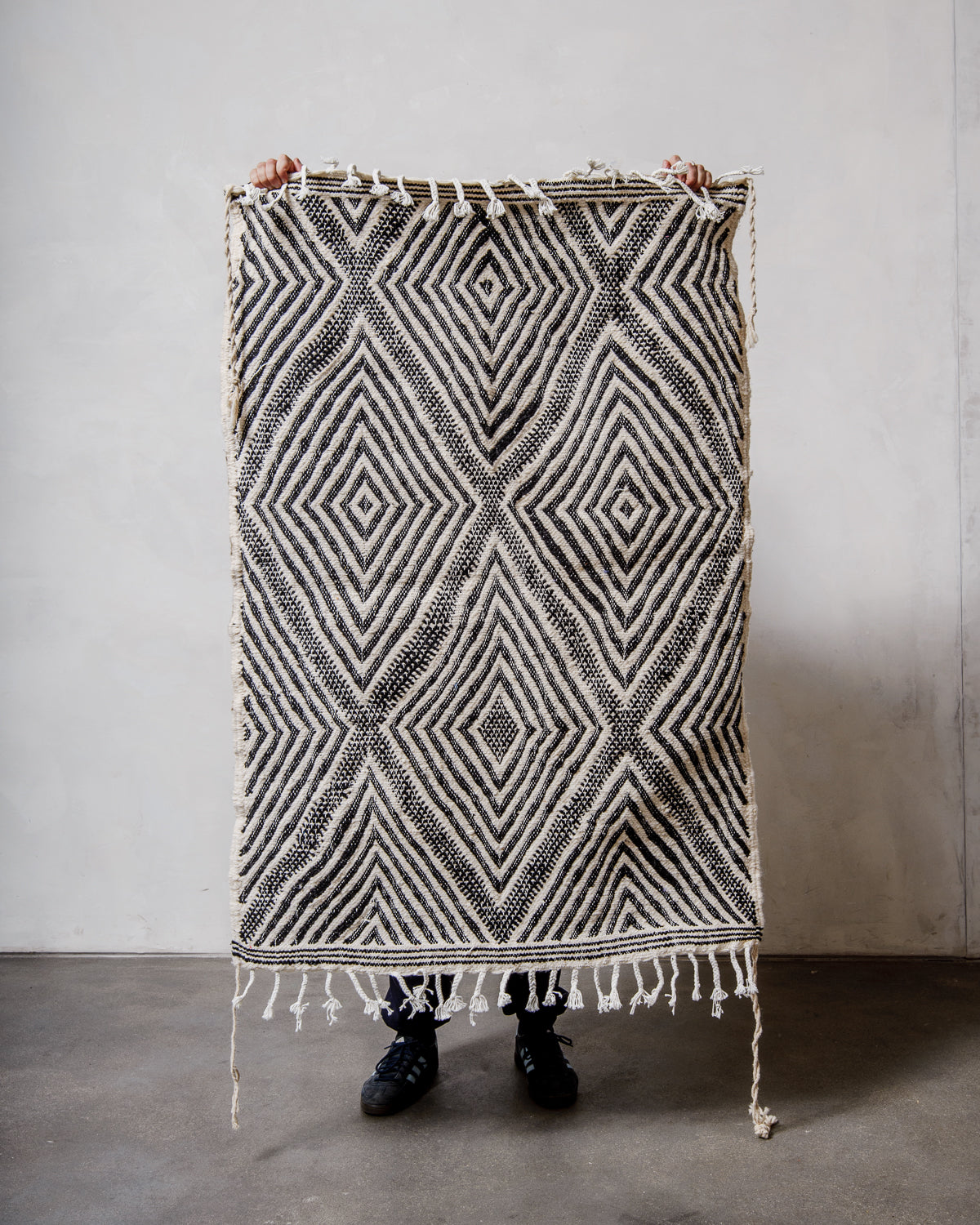 Small Berberlin Kelim Rug in black and white being held up in front of a white wall.