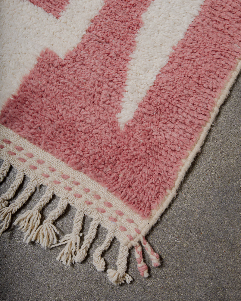 Pink and white rug with tassels on a gray surface