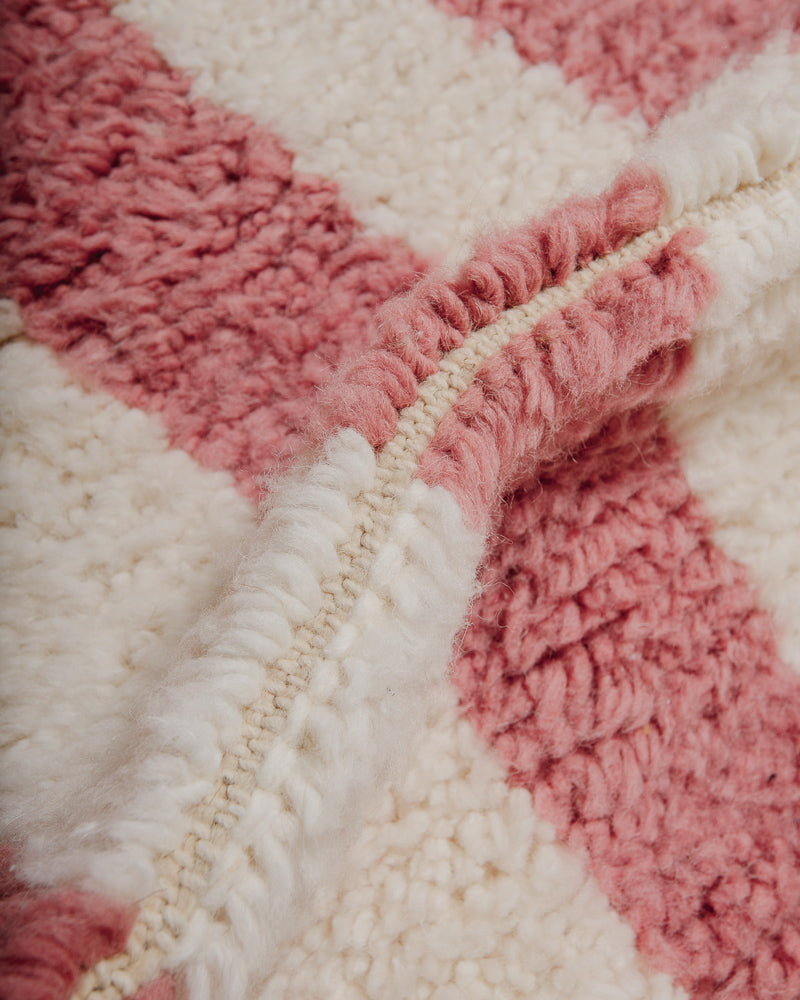 Close-up of a pink and white textured rug with fluffy wool pile.