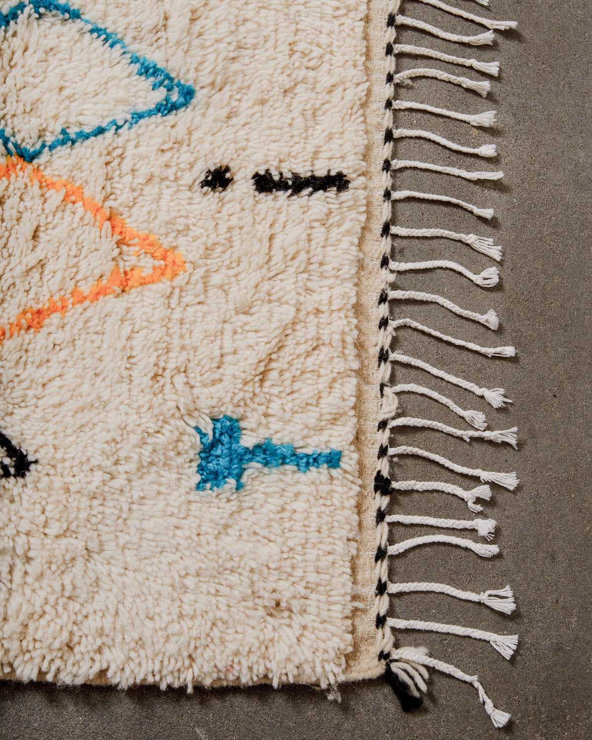 Corner of cream Azilal rug with a tightly woven edge and white cotton tassels across the end. 