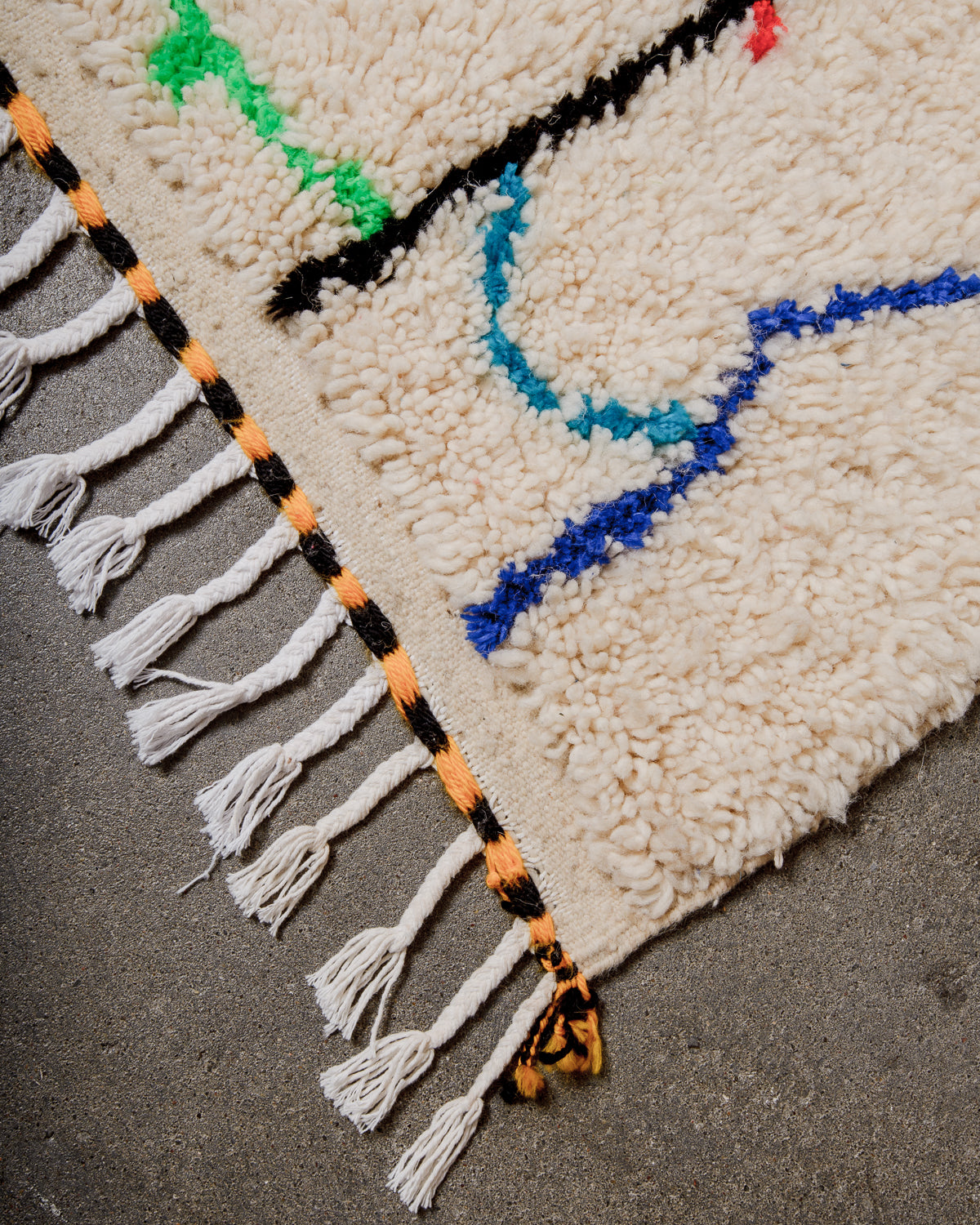 Corner of Azilal run with cream wool and white cotton tassels and black and yellow weaving across the edge.