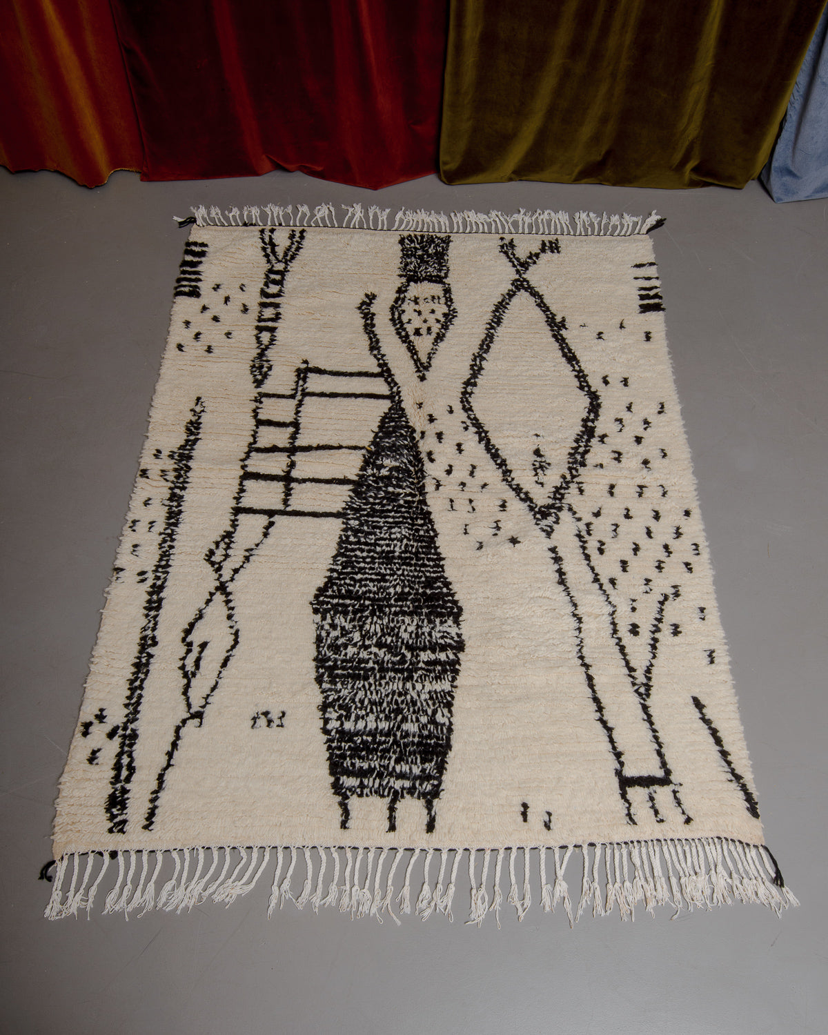 Berberlin Azilal rug with abstract design in black on grey floor in front of velvet curtains.