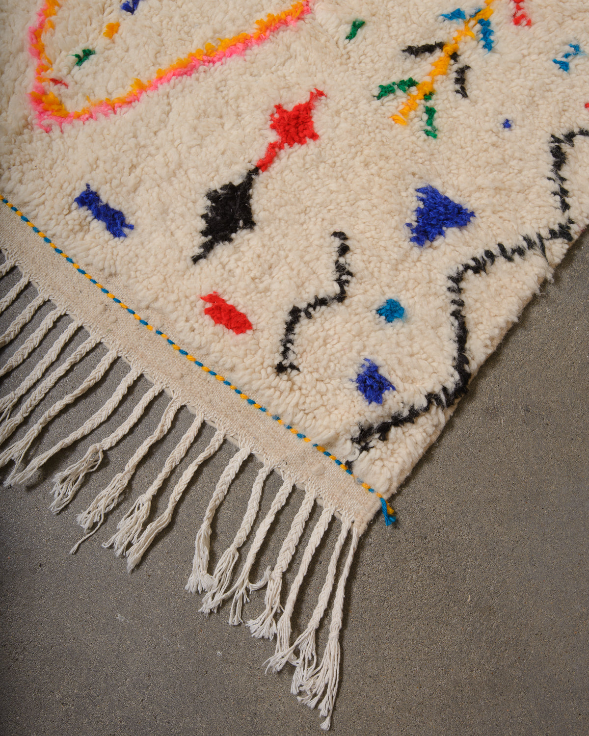 Corner of Azilal run with cream wool and white cotton tassels and blue and yellow weaving across the edge.