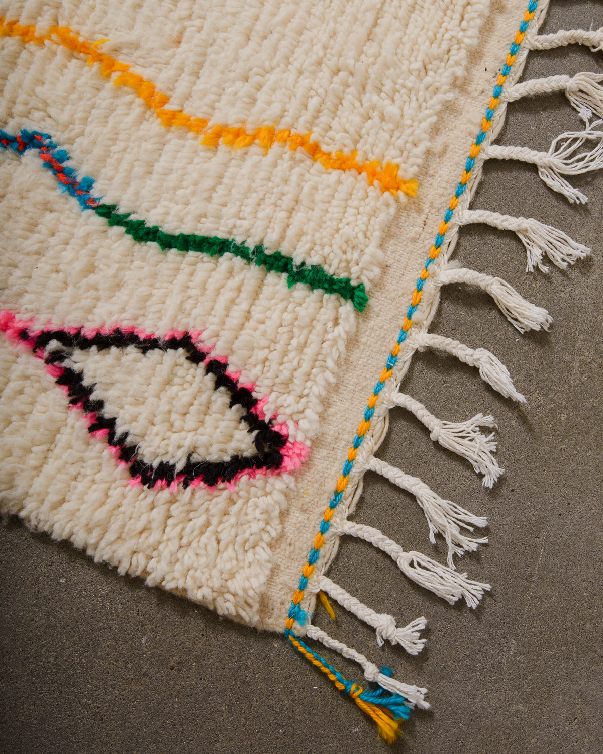 Corner of Azilal rug with cream wool and white cotton tassels and blue and yellow weaving across the edge.