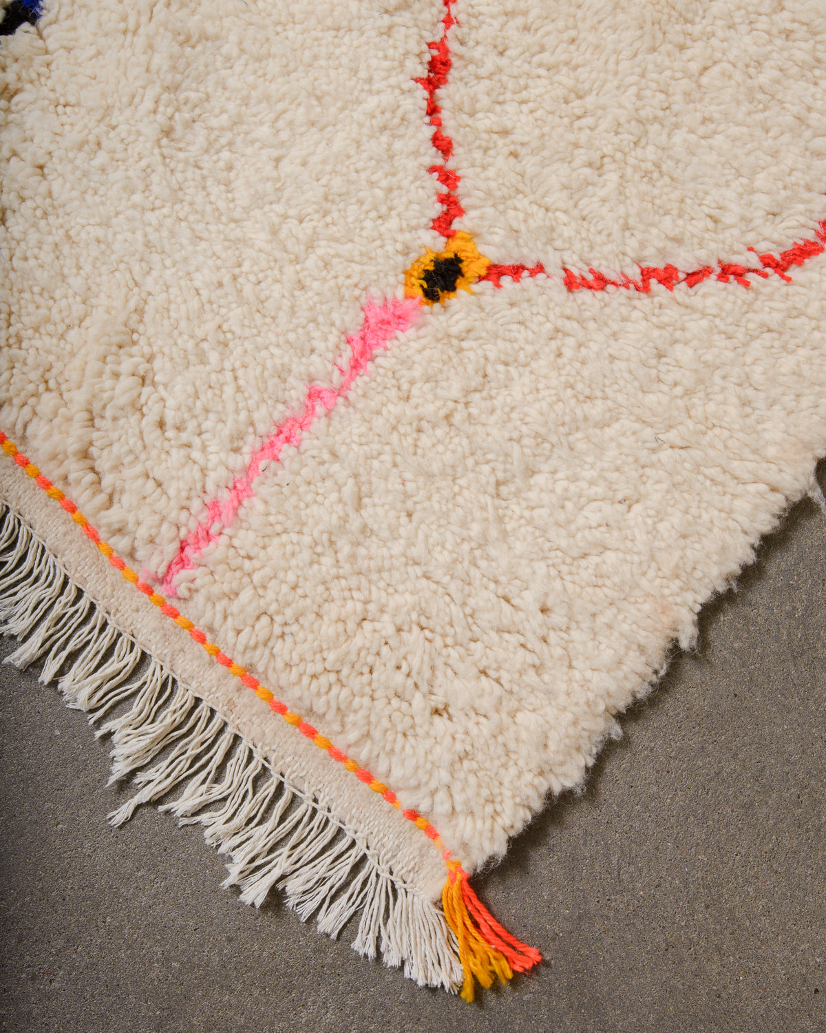 Corner of Azilal run with cream wool and colourful design and white cotton tassels across the edge with orange and yellow trim.
