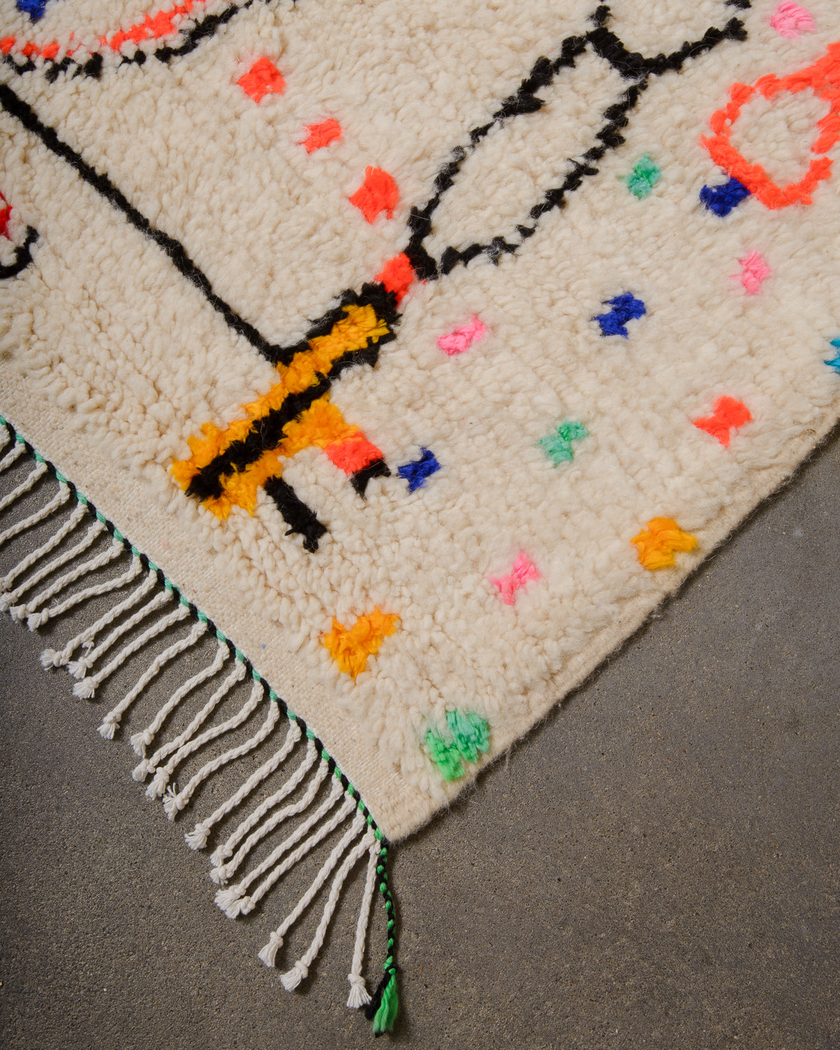 Corner of Azilal run with cream wool and white cotton tassels and black and green weaving across the edge.