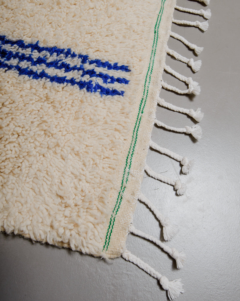 Corner of azilal rug with green stitching along the end and white cotton tassels. 