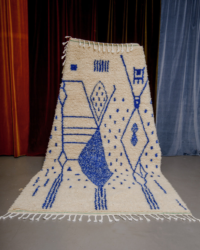 Blue and cream azilal rug held in front of velvet curtains. 