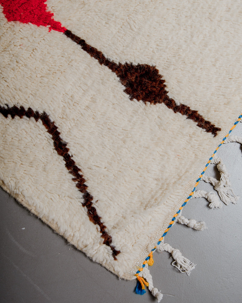 Corner of azilal rug with yellow and blue stitching along the end and white cotton tassels. 