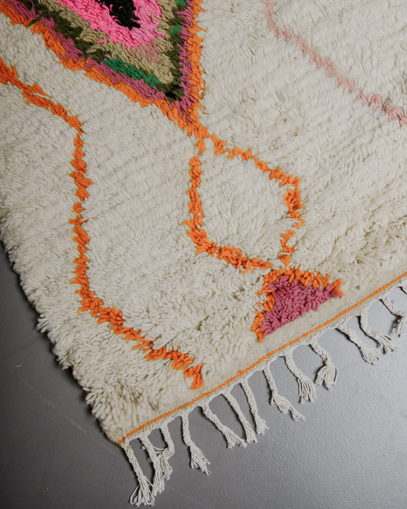 Corner of azilal rug with orange stitching along the end and white cotton tassels. 