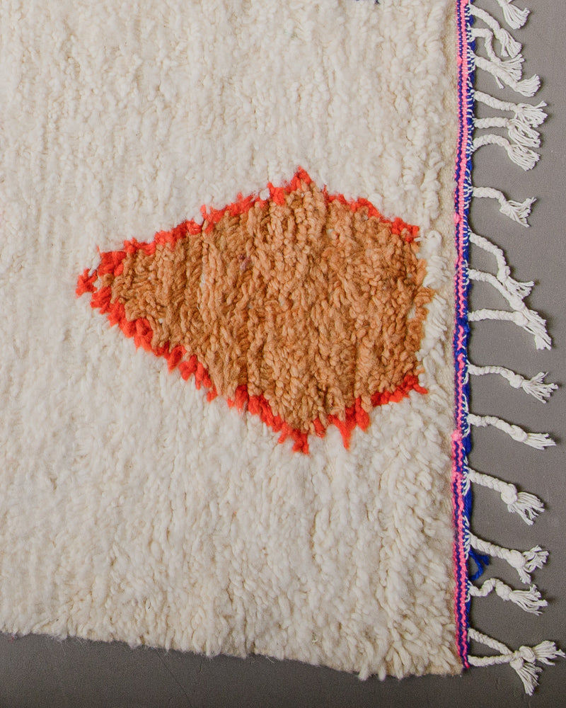 Corner of azilal rug with pink and blue stitching along the end and white cotton tassels. 