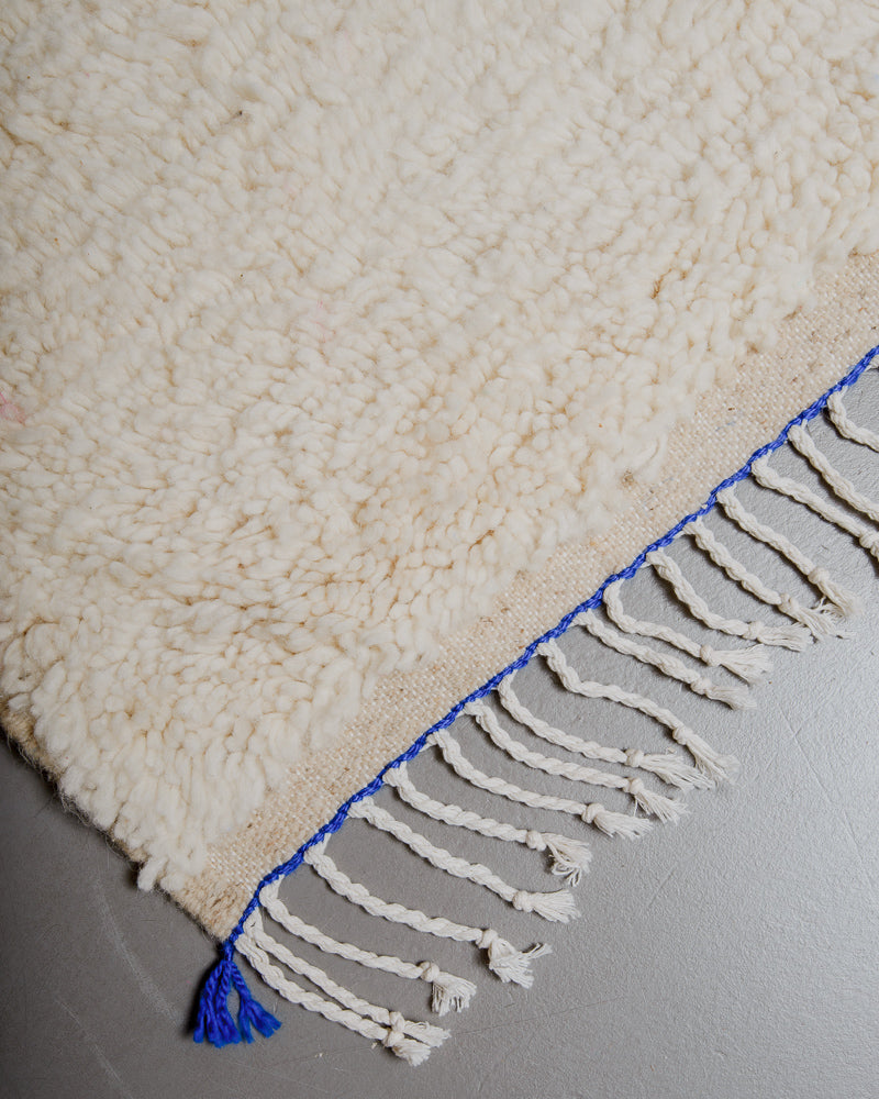 Corner of azilal rug with blue stitching along the end and white cotton tassels. 