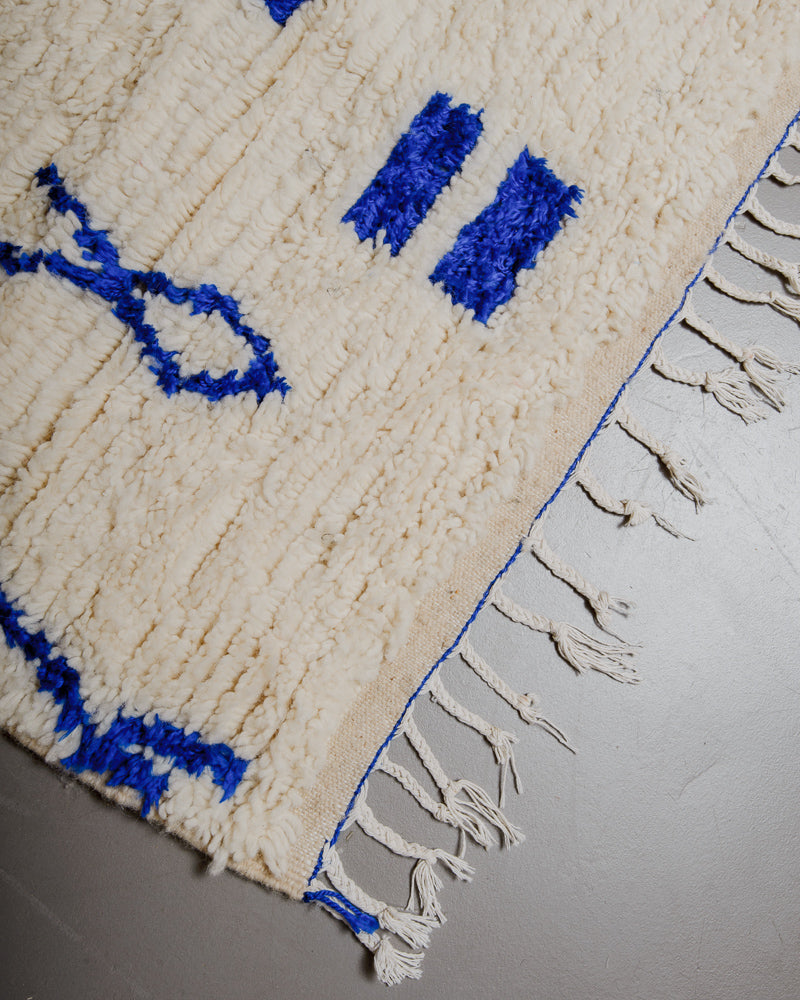 Corner of azilal rug with blue stitching along the edge and white cotton tassels. 