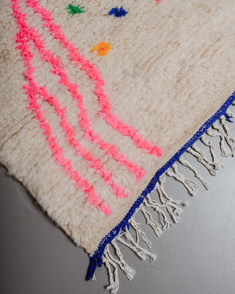 Corner of azilal rug with blue stitching along the end and white cotton tassels. 