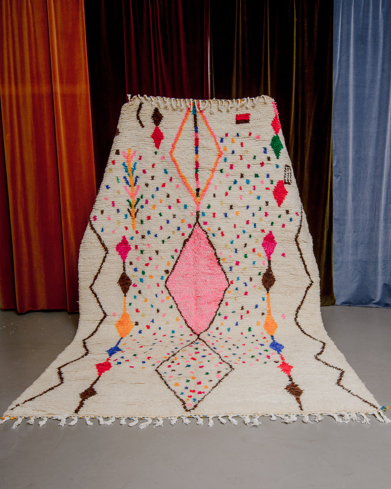 Colourful azilal rug held in front of velvet curtains. 