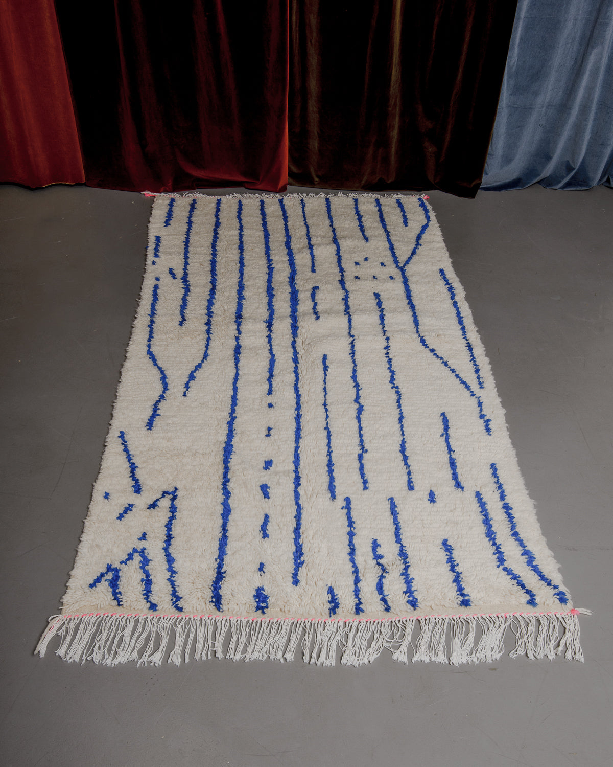 Colourful azilal rug featuring blue lines on a grey floor.