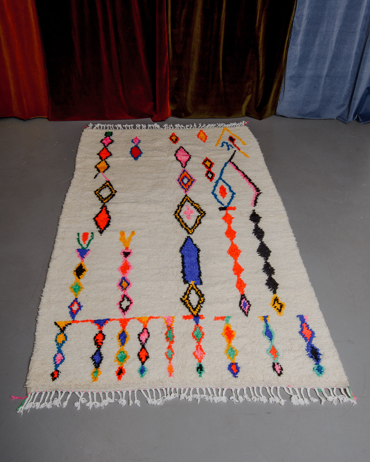Azilal rug featuring colourful design on a grey floor in front of curtains.