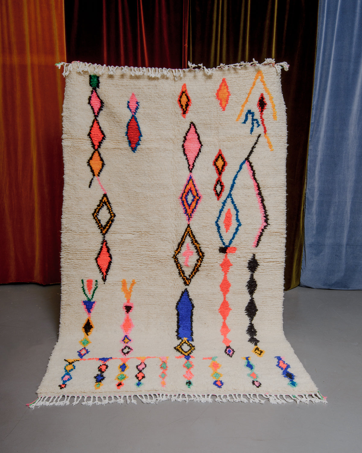 Azilal rug held in front of velvet curtains. 