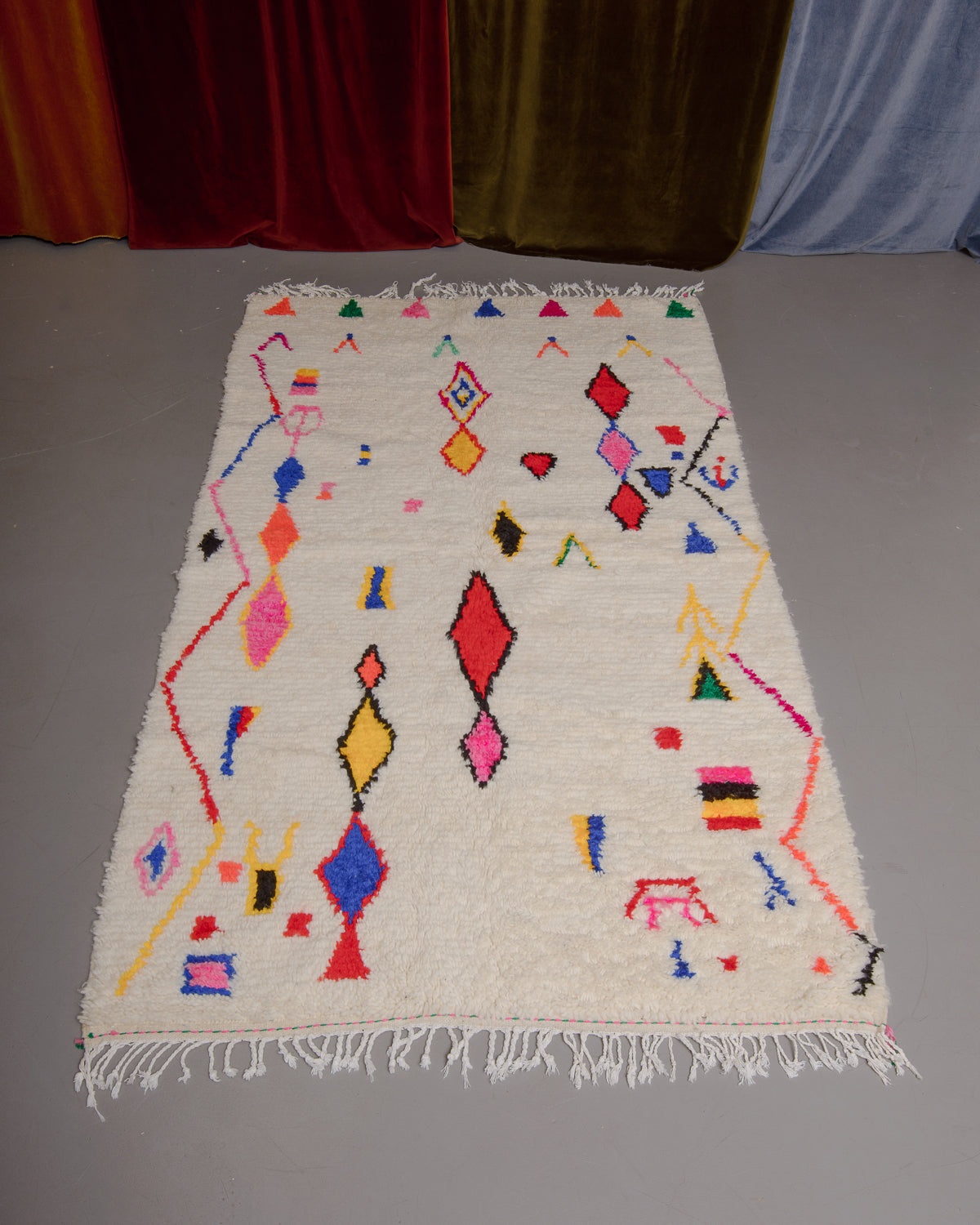 Azilal rug featuring colourful design on a grey floor in front of curtains.